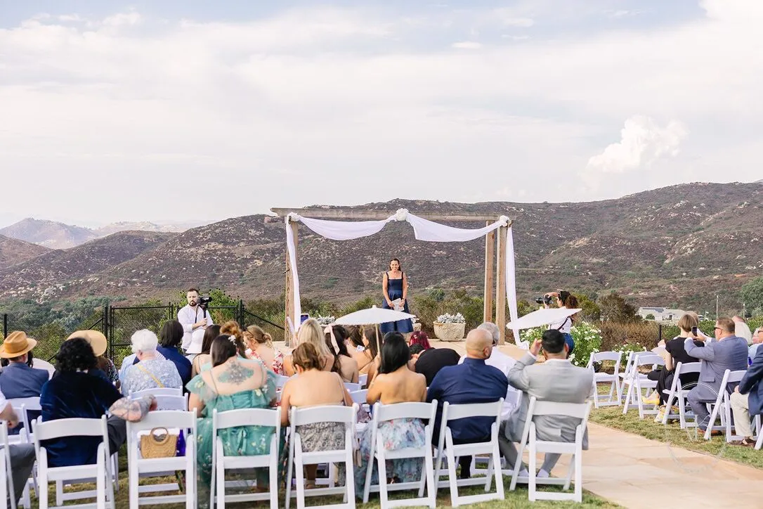Guests seated for a ceremony at the draped arbor with layered mountain ridges behind