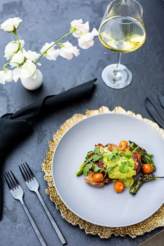 Plated dinner course on a gold charger with white wine and flowers