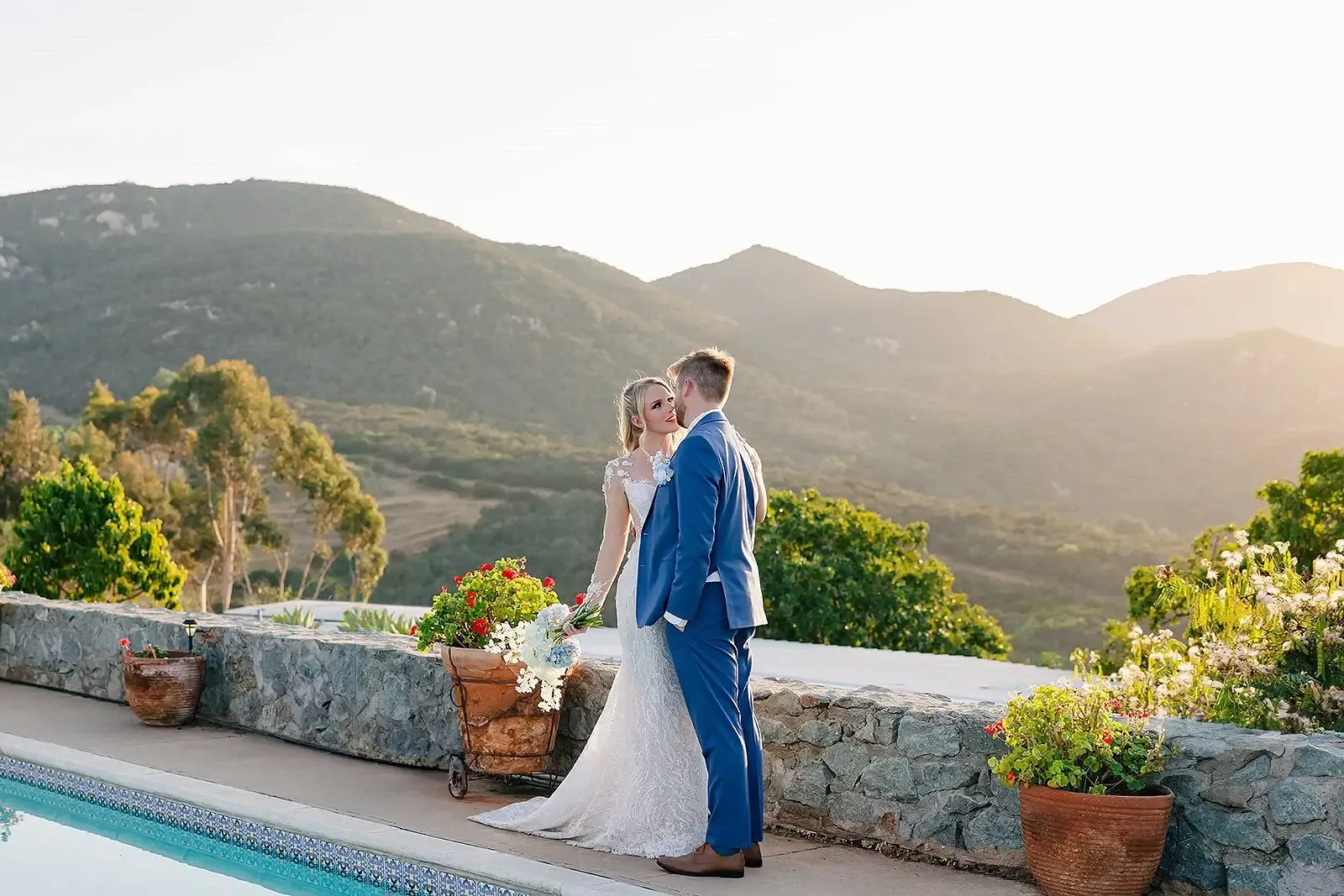 Bride and groom kissing beside the pool terrace at golden hour with the Jamul mountains behind them